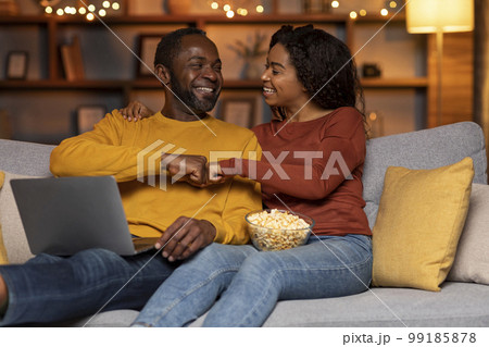 Joyful black couple sitting on couch, using laptop, gambling online 99185878