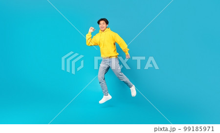 Joyful Chinese Teen Boy Jumping Smiling Posing Over Blue Background Joyful Chinese Teen Boy Jumping Smiling Posing Over Blue Background 99185971