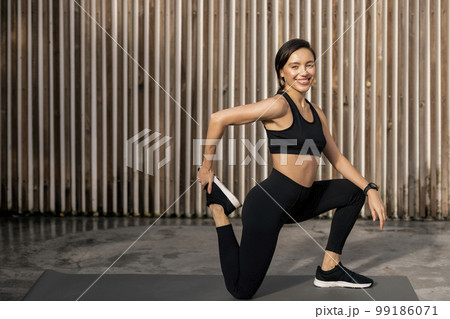Smiling slim caucasian millennial female in sportswear with fitness tracker doing leg stretching Smiling slim caucasian millennial female in sportswear with fitness tracker doing leg stretching 99186071