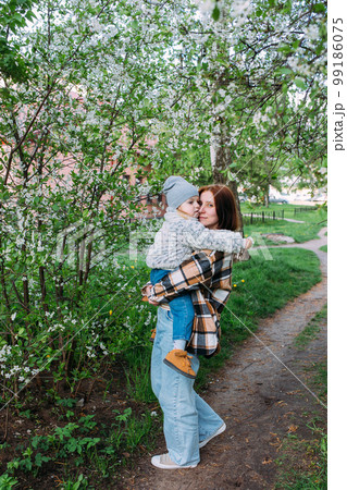 Young woman with her daughter in nature admires white flowering of spring trees Young woman with her daughter in nature admires white flowering of spring trees 99186075