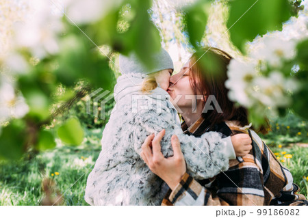 Young woman with her daughter in nature admires white flowering of spring trees Young woman with her daughter in nature admires white flowering of spring trees 99186082