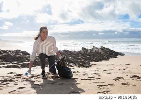Female eco volunteer picking up plastic trash on the beach, collecting garbage, protecting the planet, free space 99186085
