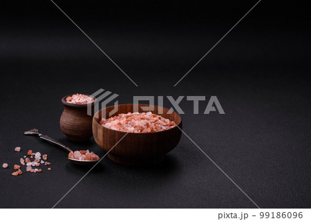 Pink himalayan salt in a wooden bowl on a dark concrete background 99186096
