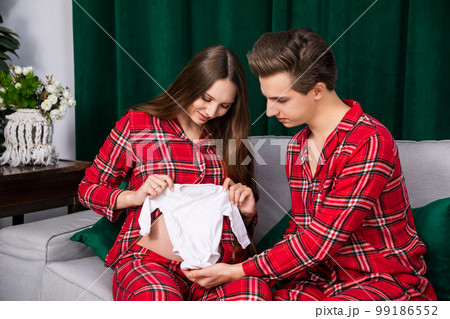 A woman and a man apply infant clothes to a pregnant belly. 99186552