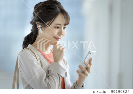 イヤホンをつけてスマートフォンを持った30代のビジネスウーマン  99190324