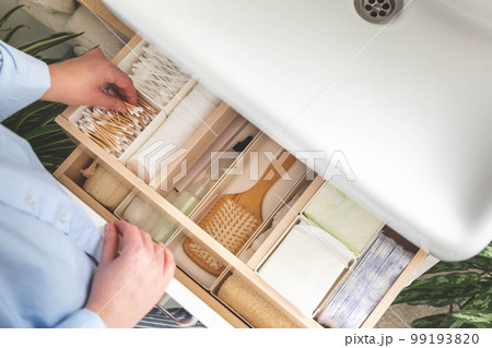 Top view of woman hands neatly organizing bathroom amenities and toiletries in drawer in bathroom. 99193820