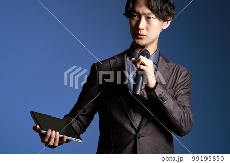 マイクとタブレットを持ってスピーチをする若いビジネスパーソン　ビジネスイメージ 99195850