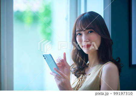 窓辺でスマホを操作する若い女性のビューティーイメージ 99197310