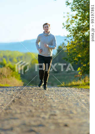 Man jogging in rural nature at beautiful summer day. Sport fitness model caucasian ethnicity training outdoor. 99197861