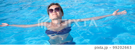 Charming woman in sunglasses enjoys swimming in turquoise water of pool Charming woman in sunglasses enjoys swimming in turquoise water of pool 99202663
