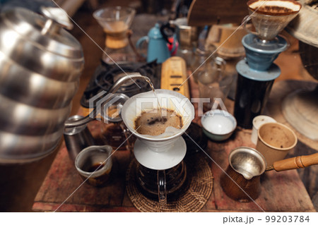 Man pouring hot water on ground coffee with paper filter to making a drip coffee Man pouring hot water on ground coffee with paper filter to making a drip coffee 99203784