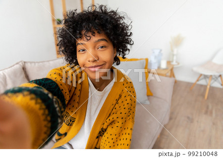 Happy african american teen girl blogger smiling face talking to webcam recording vlog. Social media influencer woman streaming making video call at home. Headshot portrait selfie webcamera view Happy african american teen girl blogger smiling face talking to webcam recording vlog. Social media influencer woman streaming making video call at home. Headshot portrait selfie webcamera view 99210048