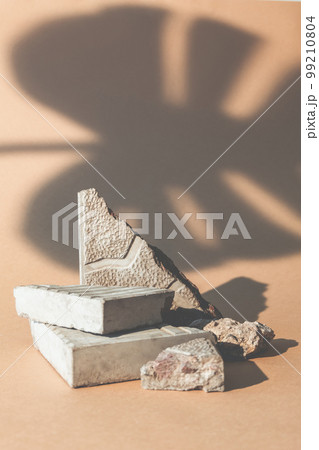 Stone showcase. Product presentation. Nature composition. Broken mineral rock pieces stand palm leaf shadow on beige empty space advertising background. Stone showcase. Product presentation. Nature composition. Broken mineral rock pieces stand palm leaf shadow on beige empty space advertising background. 99210804