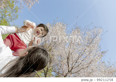 桜の咲く公園で娘を抱き上げる母親 99211258