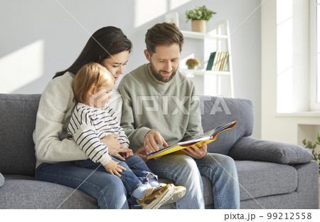 Parents and their adorable toddler baby reading book 99212558