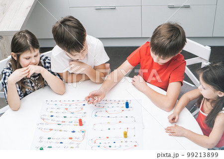 Friends play board game with dice and chips on table, from above view. Kids look at boy throw dice and move figure. Friends play board game with dice and chips on table, from above view. Kids look at boy throw dice and move figure. 99213899