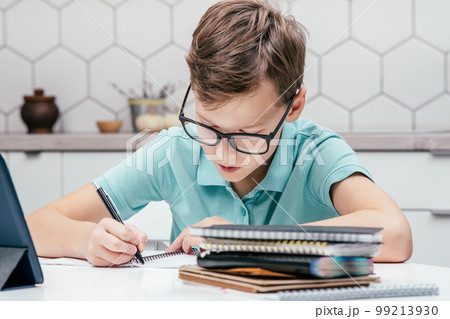 Portrait of preteen serious boy having online lesson, making notes, writing on notebook, holding pen with left hand. Portrait of preteen serious boy having online lesson, making notes, writing on notebook, holding pen with left hand. 99213930