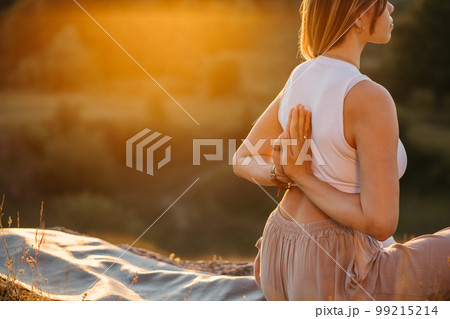 Young Woman with Folded Hands on the Back Meditating and Enjoying Beautiful Sunset Outdoors 99215214