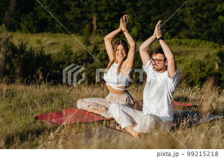 Cheerful Woman and Happy Man Raising Hands Up Over Heads, Young Adult Couple Meditating Outdoors in the Nature Cheerful Woman and Happy Man Raising Hands Up Over Heads, Young Adult Couple Meditating Outdoors in the Nature 99215218