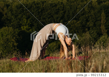Young Woman Doing Bridge Exercise During Yoga Practice Outdoors with Beautiful Background 99215312