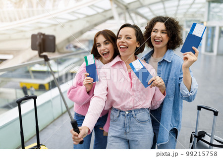 Three cheerful female friends taking selfie on smartphone at airport 99215758