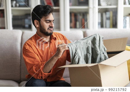 Disappointed middle eastern man customer opening parcel at home 99215792