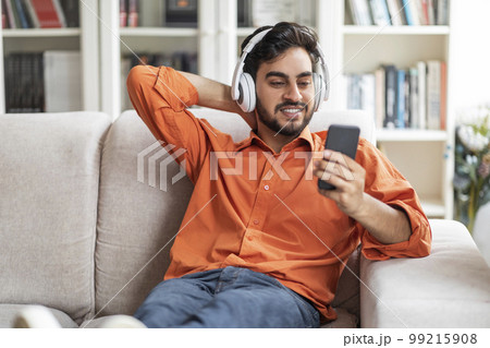 Positive arab guy chilling on couch at home, watching video 99215908