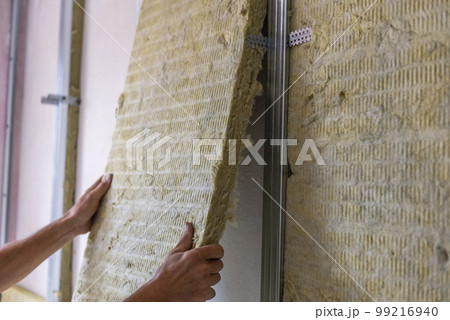 Worker insulating a room wall with mineral rock wool thermal insulation. 99216940