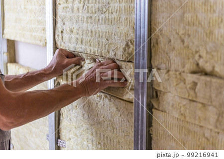 Worker insulating a room wall with mineral rock wool thermal insulation. 99216941