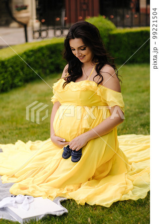 Beautiful woman is sitting on a plaid on the grass. Elegant pregnant woman waiting for baby. Future mom. Yeallow dress 99221504