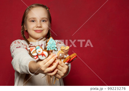 Christmas concept. Sweet xmas cookie gingerbread food in hands of child girl on red studio wall 99223276
