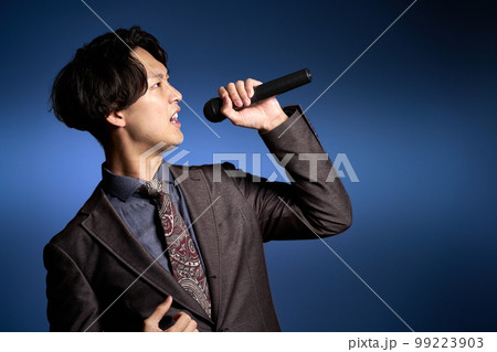 マイクを持って大声を出すスーツ姿の若い男性 99223903