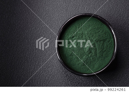 Spice, green color spirulina in the form of powder in a black bowl 99224261