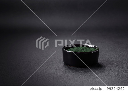 Spice, green color spirulina in the form of powder in a black bowl 99224262