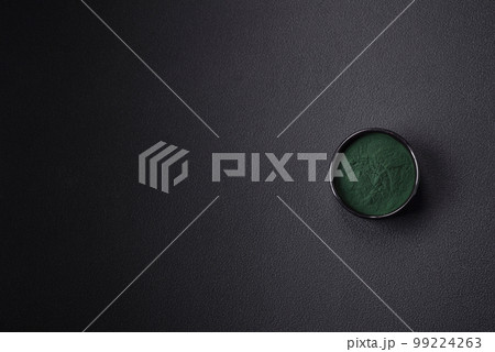 Spice, green color spirulina in the form of powder in a black bowl 99224263