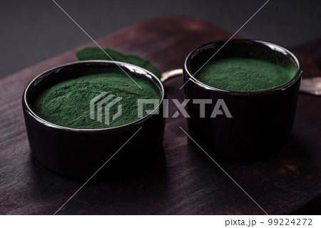 Spice, green color spirulina in the form of powder in a black bowl Spice, green color spirulina in the form of powder in a black bowl 99224272