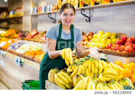 Positive female seller with ripe bananas on supermarket 99228666