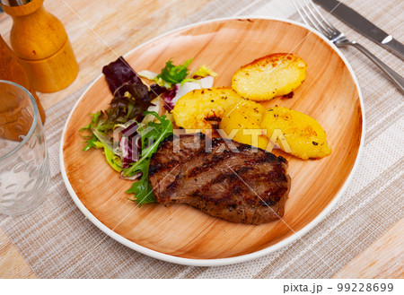 Grilled beef steak with baked potato slices garnished with greens Grilled beef steak with baked potato slices garnished with greens 99228699