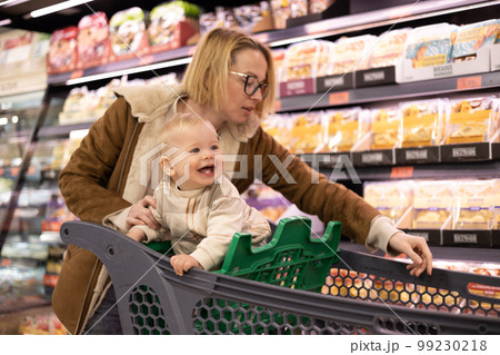 Caucasian mother shopping with her infant baby boy child choosing products in department of supermarket grocery store Caucasian mother shopping with her infant baby boy child choosing products in department of supermarket grocery store 99230218