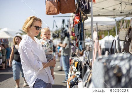 Mother hoding his infant baby boy child whilechecing items at sunday flea market 99230228
