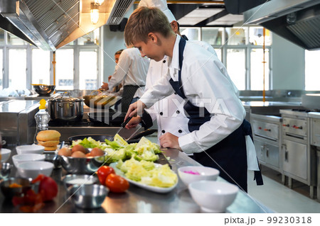 Chef teacher teaches cooking to the group children in class kitchen room. Chef teacher teaches cooking to the group children in class kitchen room. 99230318