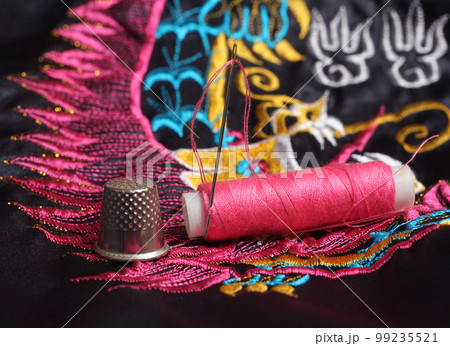 Spool of Pink Thread and Thimble on Vintage Pink and Black Satin Fabric 99235521
