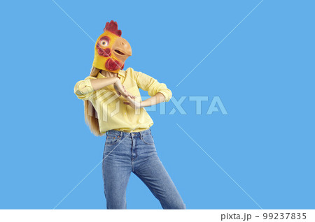 Young woman wearing funny strange chicken mask dancing on blue studio background Young woman wearing funny strange chicken mask dancing on blue studio background 99237835