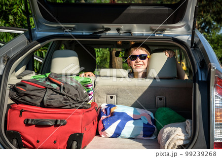 Adorable kid boy wearing sunglasses sitting in car trunk. Portrait of Happy child with open car boot while waiting for parent get ready for vocation. Family trip traveling by car concept 99239268