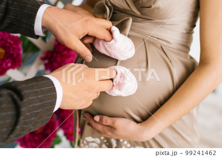 Male hands of a woman put on shoes for youth and hold them near the pregnant belly Male hands of a woman put on shoes for youth and hold them near the pregnant belly 99241462