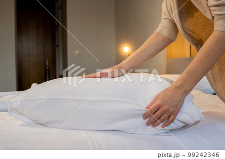 Woman fluffing soft pillow in bedroom. Woman with her hands fluffs up a pillow lying on the bed 99242346