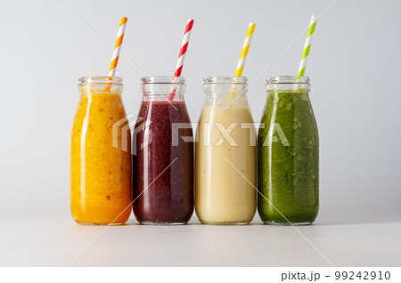 Bottles with fruit smoothies and colourful straws. Healthy detox drinks, bright background 99242910