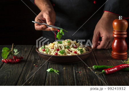 Cook adds greens to a bowl of spaghetti in the kitchen. Delicious pasta with vegetables and spices 99243932