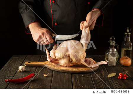Cooking chicken in the restaurant kitchen. The chef cuts raw chicken with a knife. European cuisine 99243993