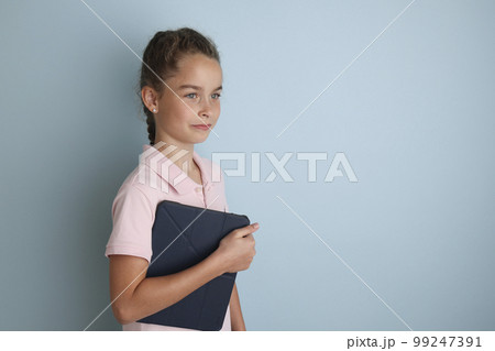Little emotional teenage girl in pink shirt 11, 12 years old on an isolated blue background with a tablet in her hands.Children's studio portrait. Place the text to copy the place for the inscription Little emotional teenage girl in pink shirt 11, 12 years old on an isolated blue background with a tablet in her hands.Children's studio portrait. Place the text to copy the place for the inscription 99247391